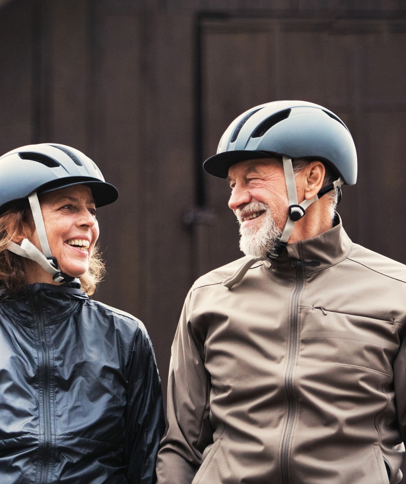 An older couple in cycling helmets laugh together.